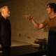 Emperor Cleon angrily addresses Hari Seldon as the robot Dermerzel watches in a plain room.